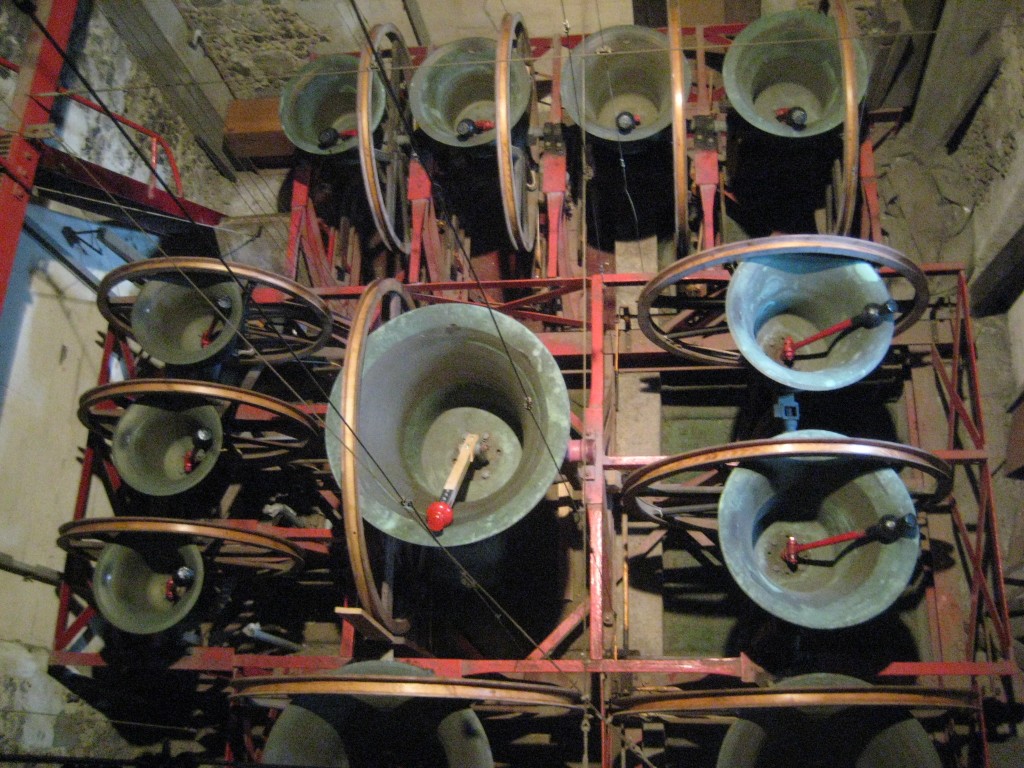 View of the bells from above. The tenor is in the centre, 1, 2 and 3 on the left of the picture,  4, 5, 6 and 7 at the top, 8 and 9 on the right, and 10 and 11 out of view at the bottom.  Note the wooden clapper shaft on the tenor.
