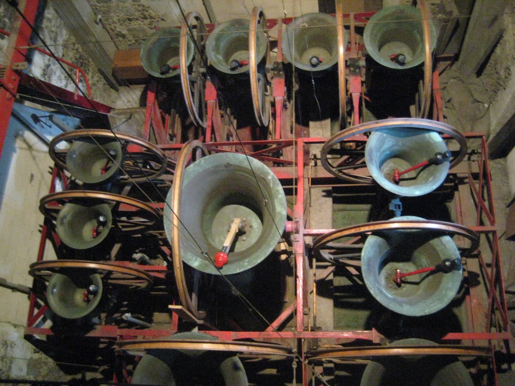 View of the bells from above. The tenor is in the centre, 1, 2 and 3 on the left of the picture,  4, 5, 6 and 7 at the top, 8 and 9 on the right, and 10 and 11 out of view at the bottom.  Note the wooden clapper shaft on the tenor.